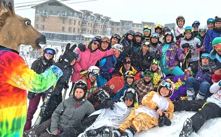 Members of Columbia's Ski and Snowboard Club, all wearing colorful gear, pose in the snow.